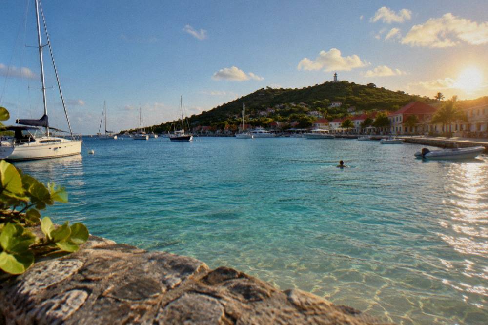 Clear shallow water over sand seen from above, with a swimmer in the distance