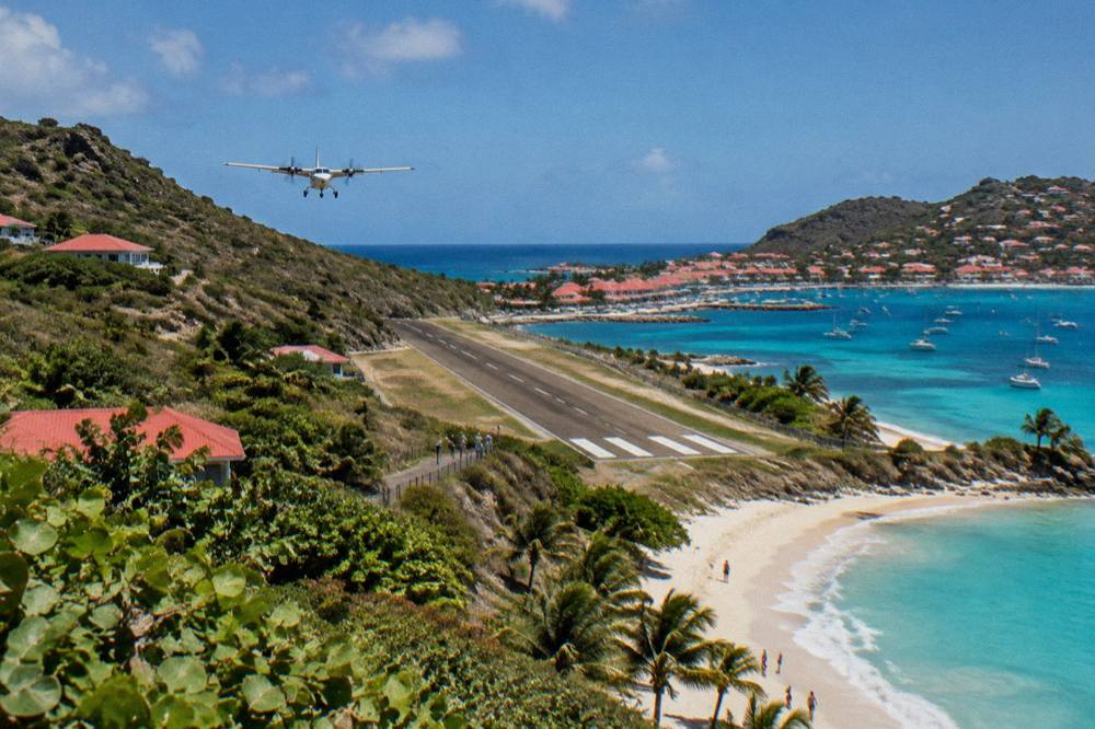 A small propeller aircraft on a short runway between a hill and a beach