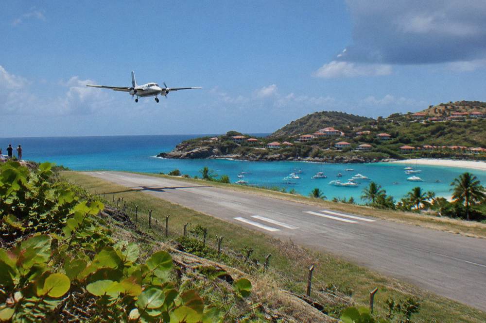 A small turboprop aircraft on a short runway beside a beach and blue sea