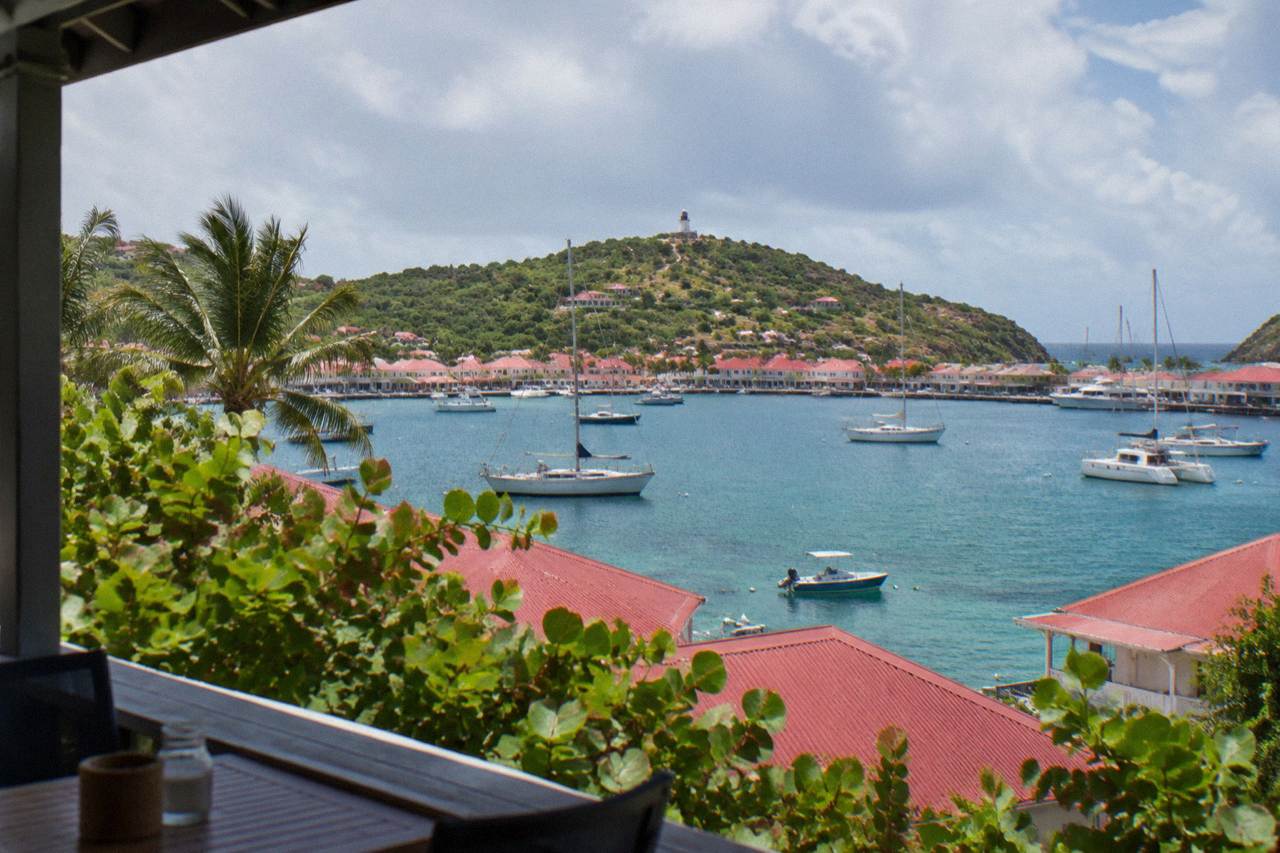 A view over red rooftops and sailboats in a Caribbean harbor under a partly cloudy sky