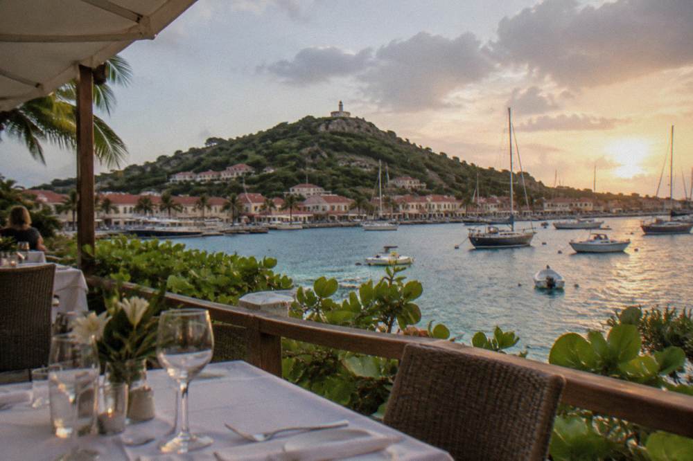A terrace restaurant with white tablecloths overlooking a harbor at dusk