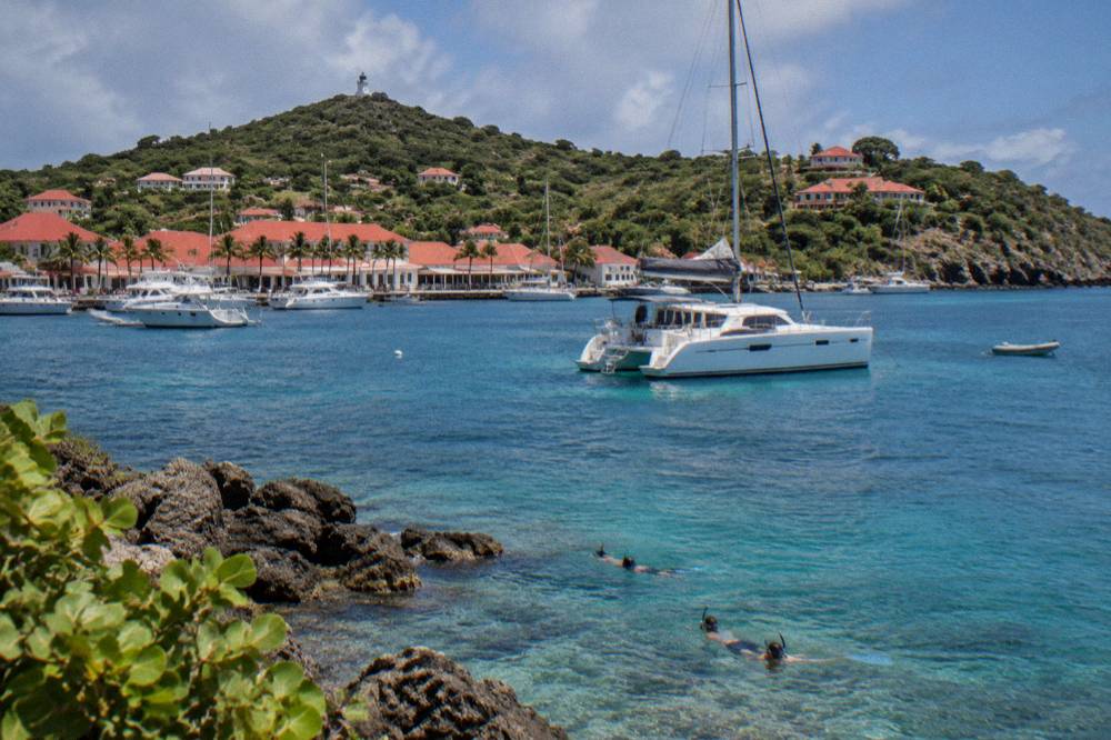 A catamaran anchored in a quiet bay with snorkelers near rocky shore