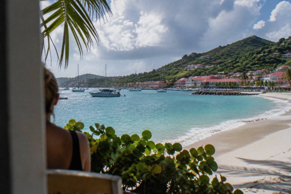 An empty crescent of pale sand and clear shallow water at a bay on St Barts under scattered clouds