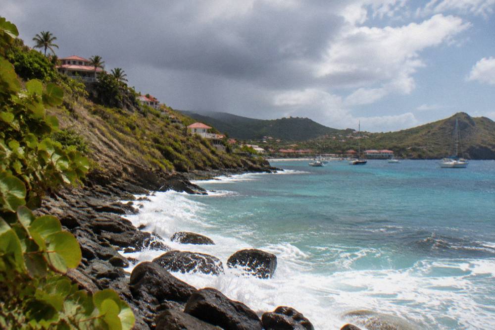 Dark rain clouds passing over green hills above a Caribbean bay with sunlight on the water