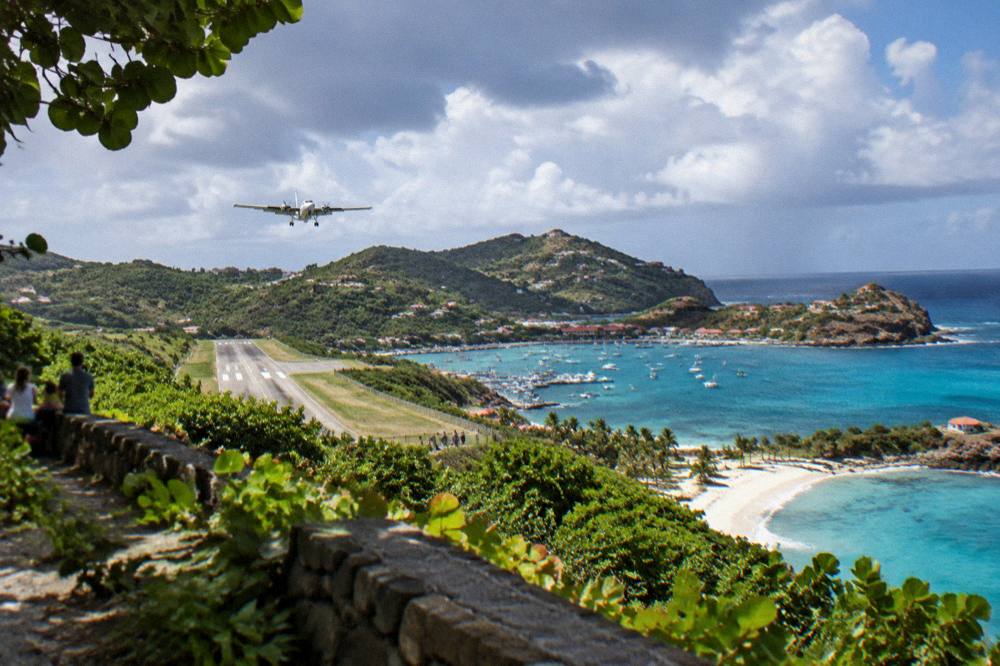 A small turboprop aircraft on a short runway sloping down toward a Caribbean bay