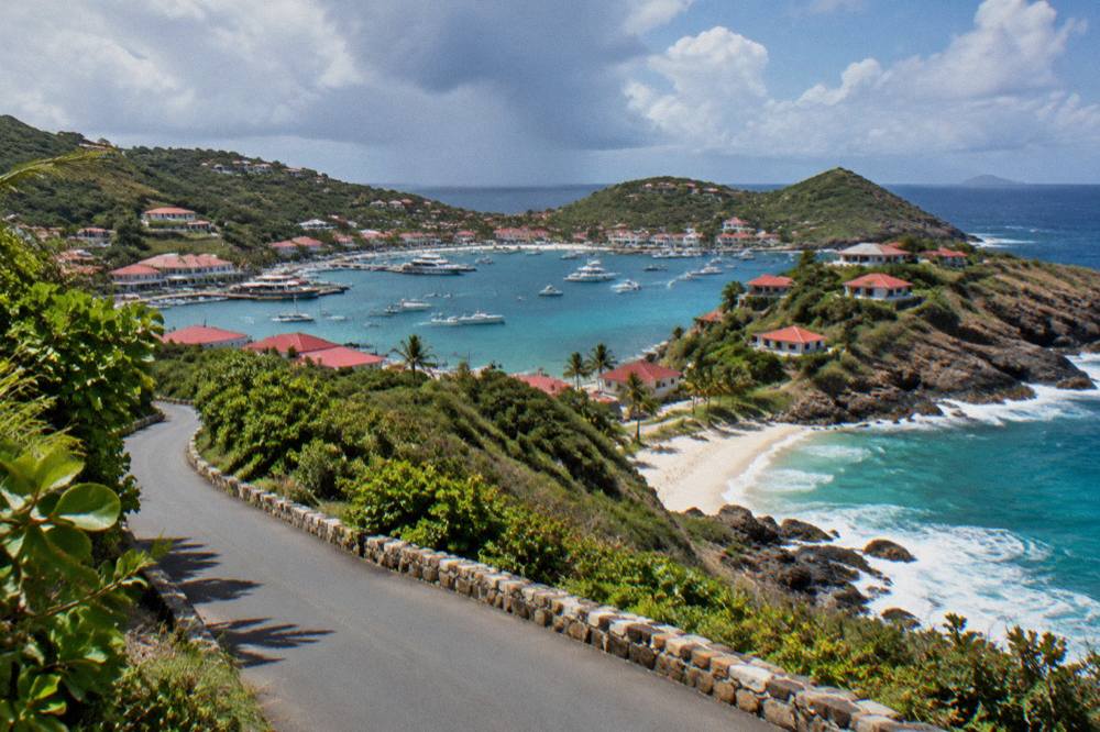 A narrow island road curving between green hillsides with sea glimpses beyond