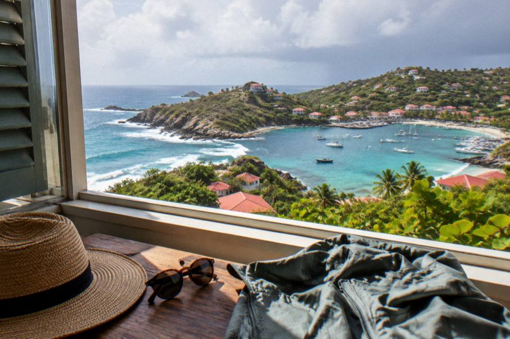 A laid-out packing scene with a sun hat, sunglasses and a light rain jacket beside an open window