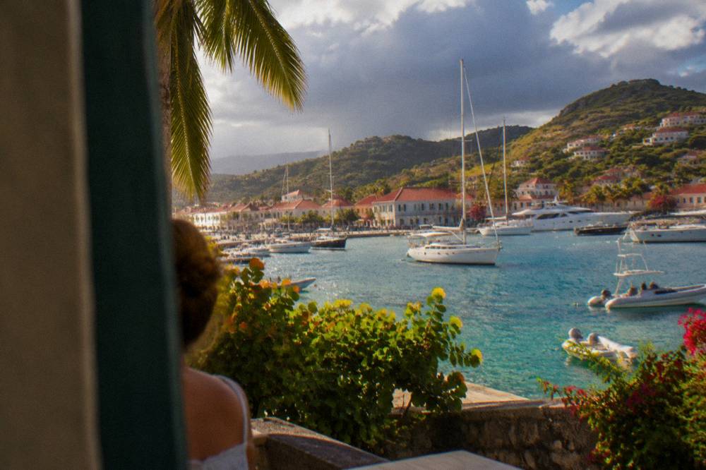 Dark rain clouds passing over green hills above a Caribbean bay with anchored sailboats