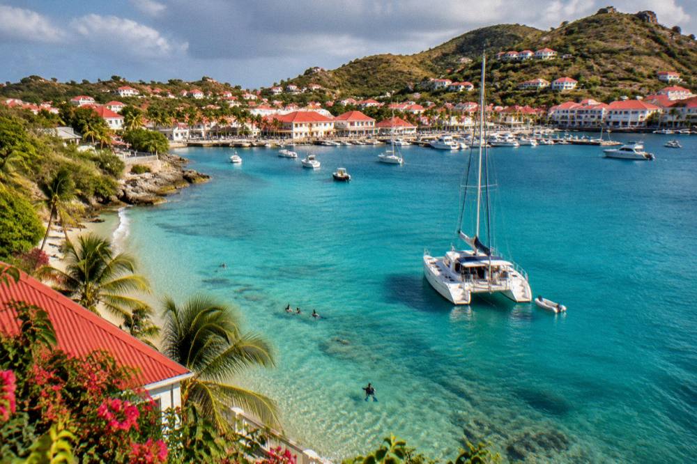 A catamaran anchored in clear turquoise water with people snorkelling near the shore
