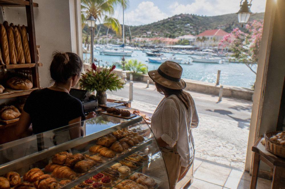 Two people chatting across a bakery counter in a small French-style shop on St Barts
