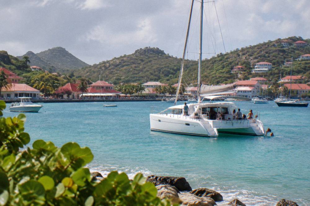 A catamaran at anchor in a turquoise Caribbean bay with passengers near the shore