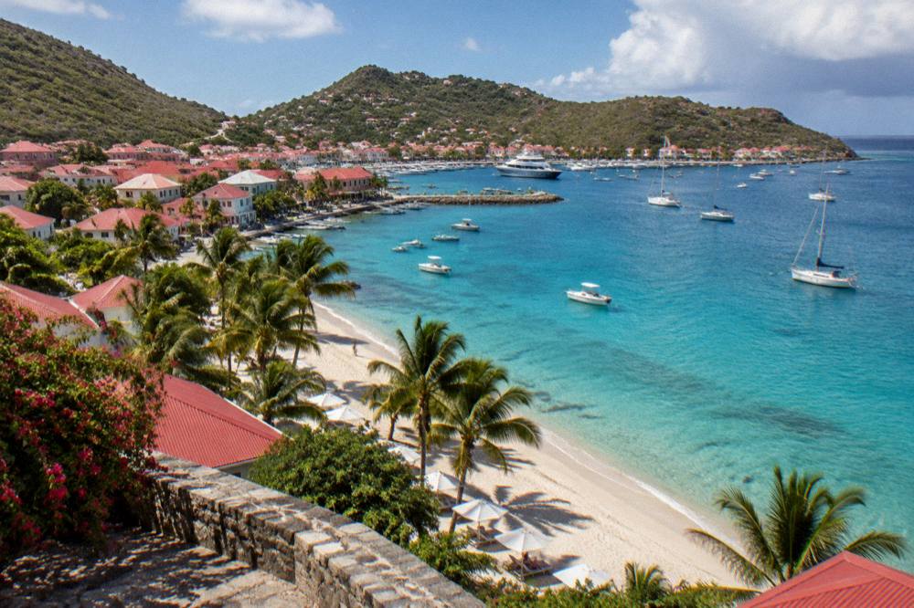 A palm-lined Caribbean beach with calm turquoise water and a few umbrellas at midday