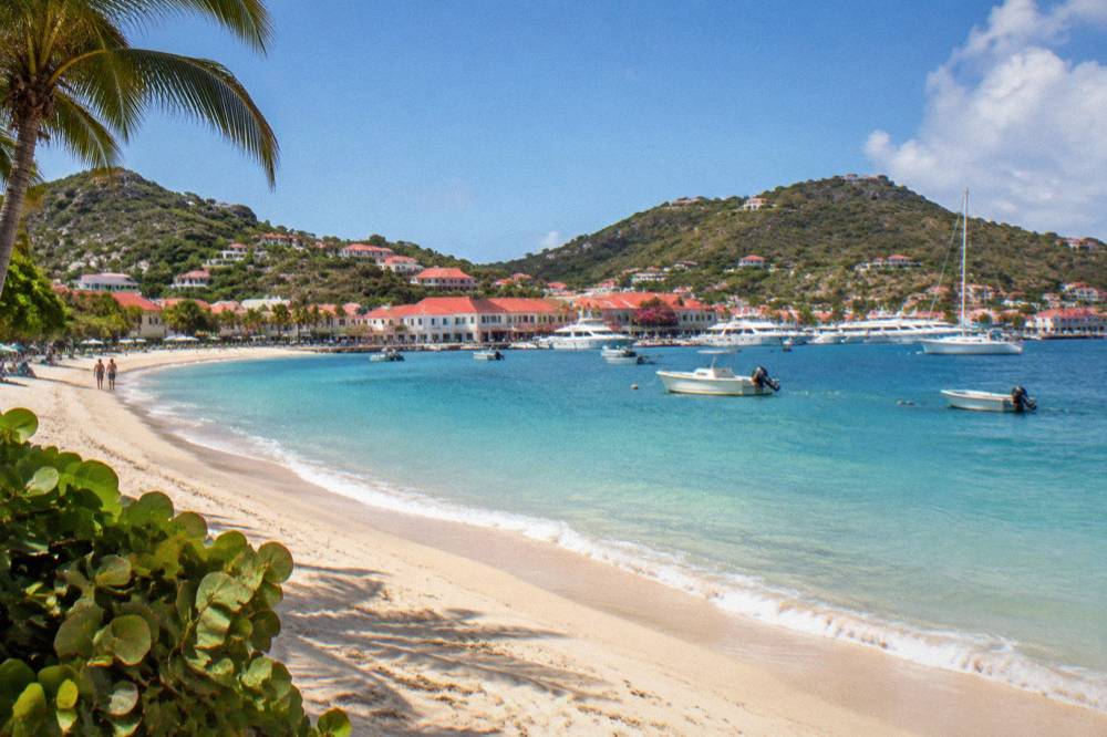 A wide sandy beach curving between green headlands on the coast of St Barts