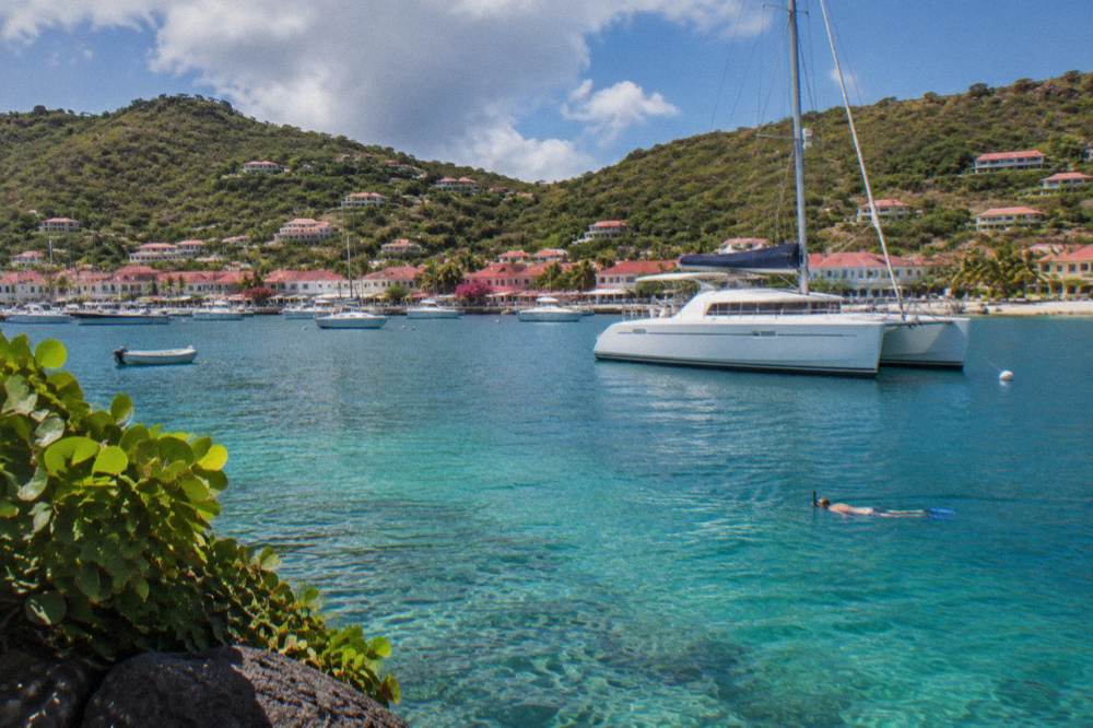 A catamaran moored in a quiet bay with a snorkeler visible in clear water