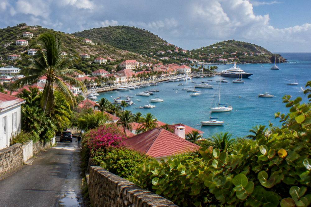 A narrow road winding between low buildings and tropical vegetation on a St Barts hillside