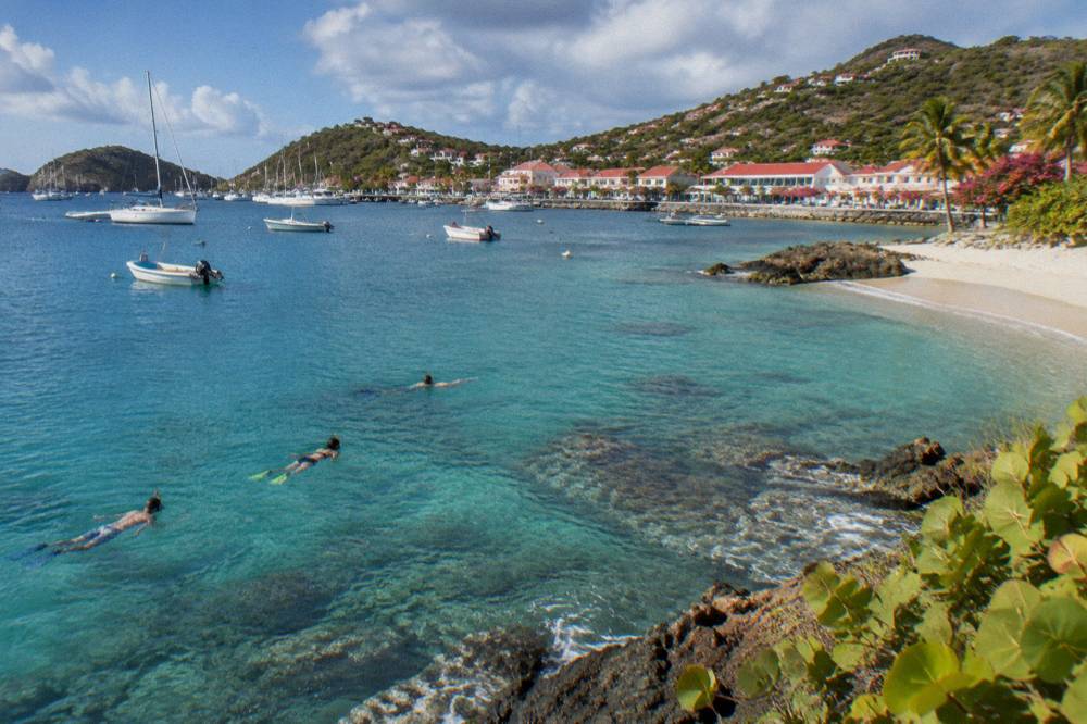 Snorkelers floating over coral and rocks in clear green water near a rocky point