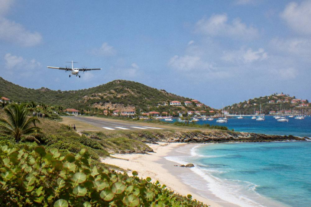 A small white turboprop aircraft on a short runway between a hill and a beach