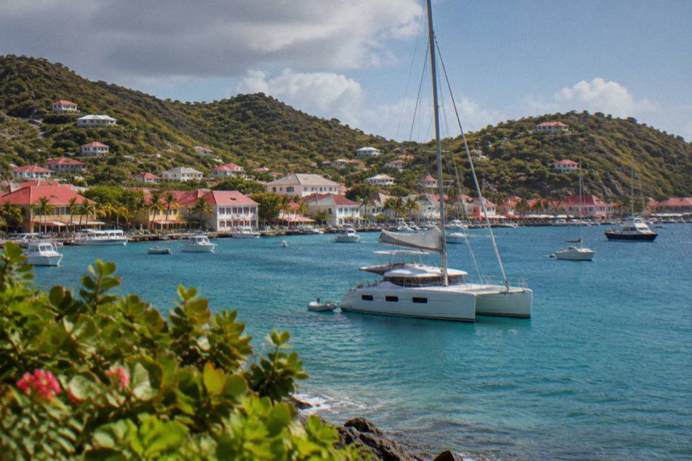 A sailing catamaran anchored in a green bay ringed by low hills