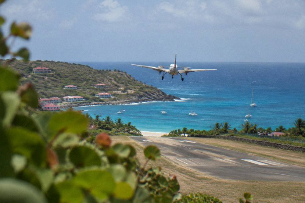 A small plane taking off from a short runway toward blue Caribbean water