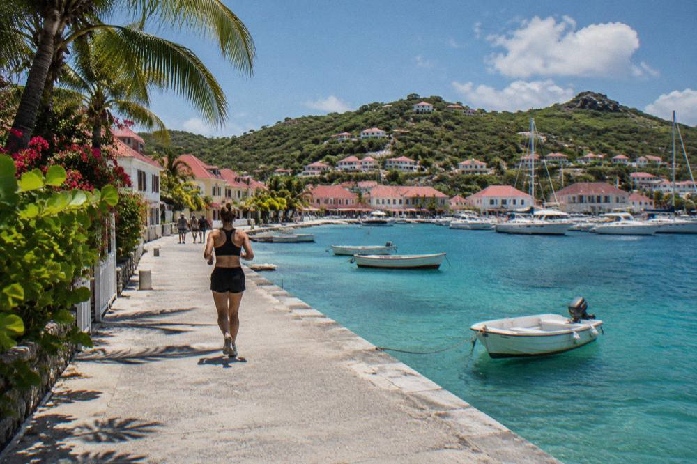 White-sand beach with calm shallow turquoise water and a few low buildings behind palms
