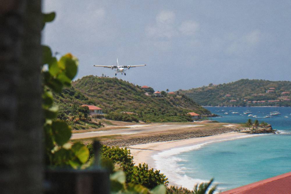 Small white turboprop aircraft on a short runway beside a beach and green hill