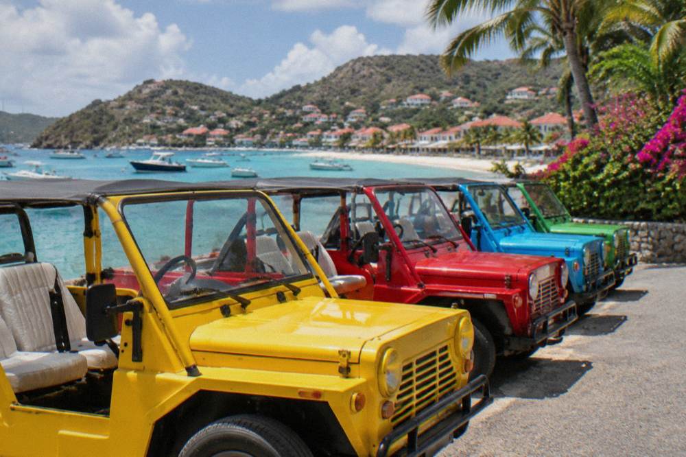 A row of parked Mini Mokes in bright colors at a rental yard near the airport