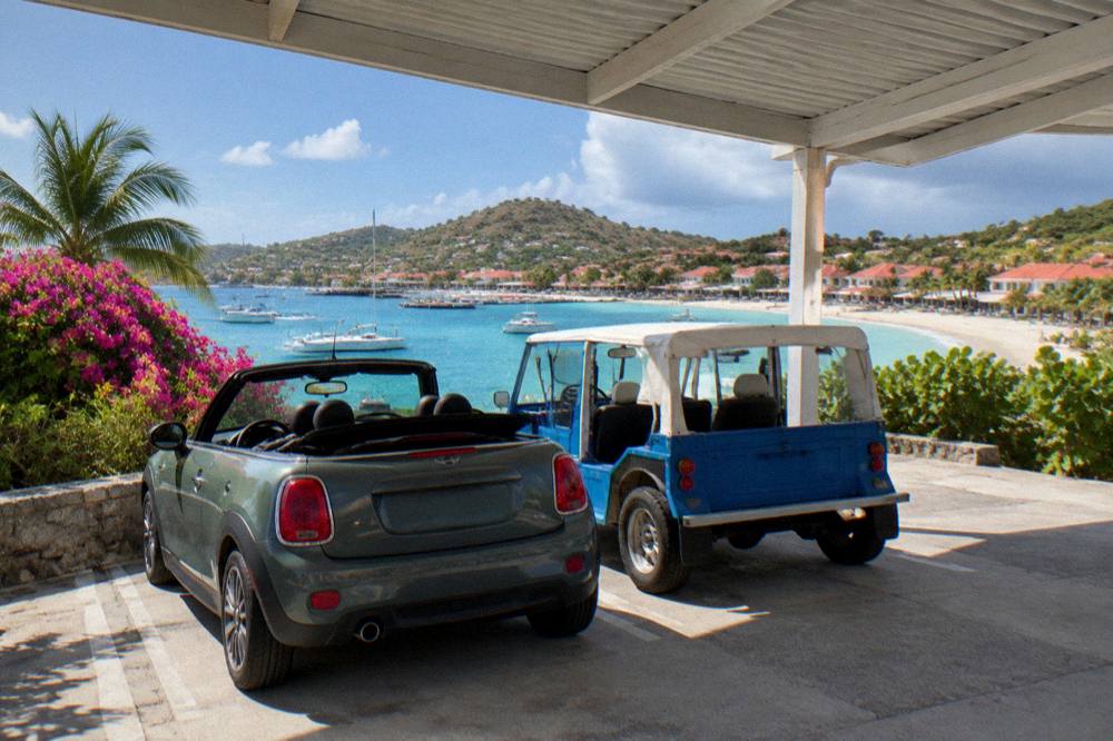 A covered parking area with a small convertible car and a Mini Moke parked side by side
