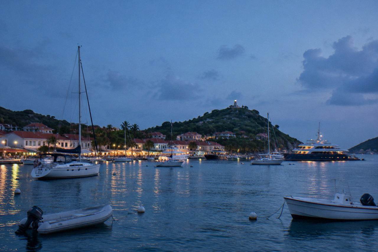 Yachts anchored in Gustavia harbor at dusk with lights along the waterfront