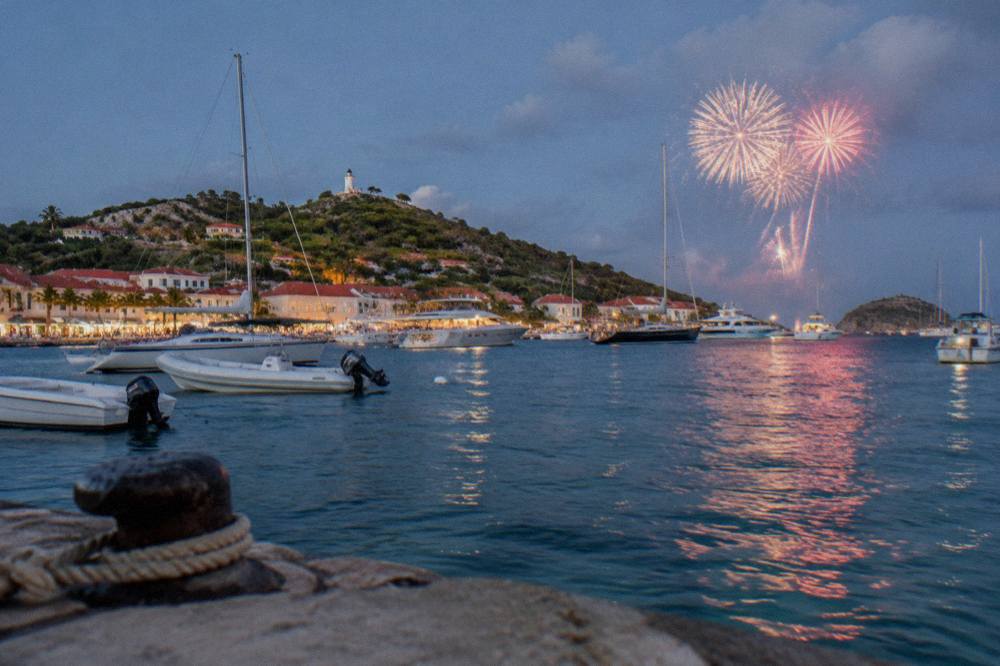 Fireworks bursting over a Caribbean harbour with boats lit up below
