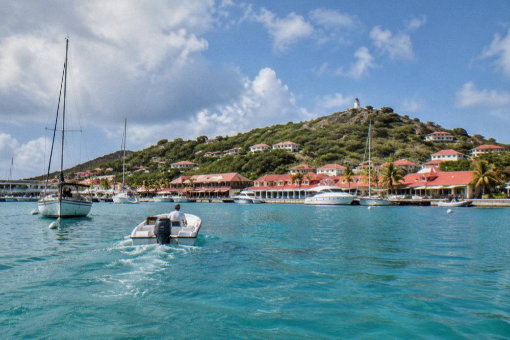 A small boat crossing calm turquoise water toward a green island coastline