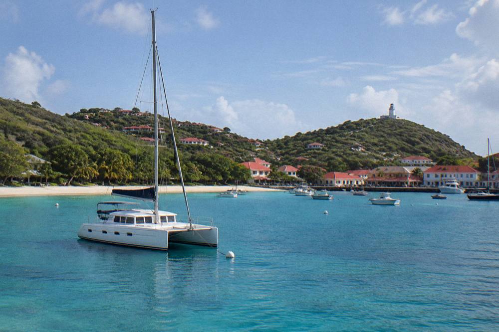 A catamaran at anchor in a quiet bay at first light with a beach behind it