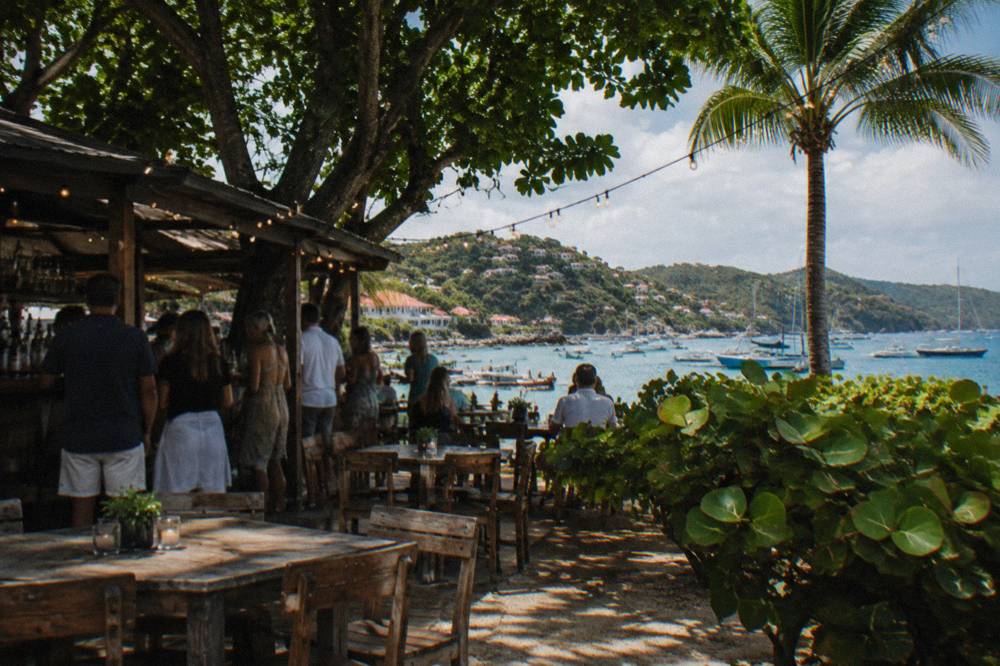 A small crowd gathered at an outdoor bar with string lights above wooden tables at night