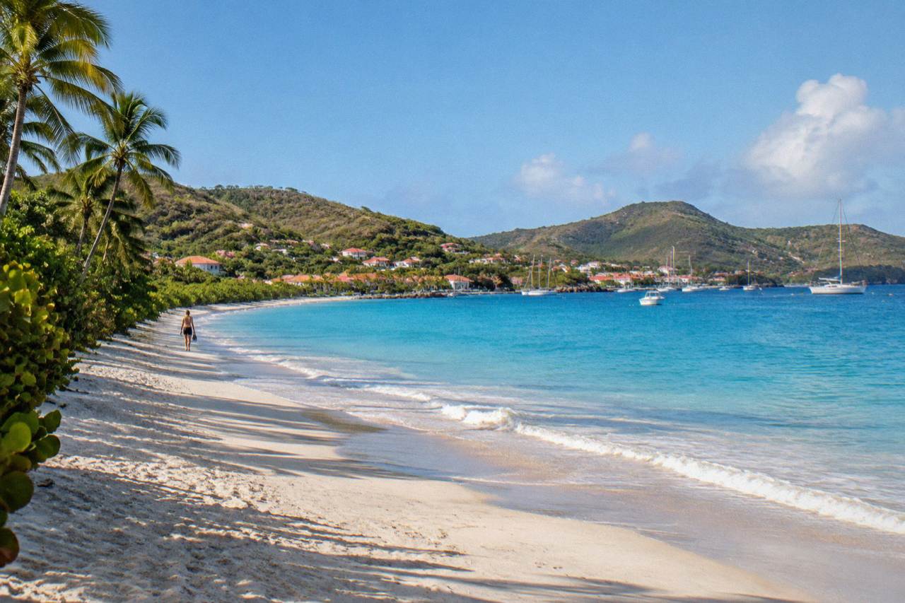 A wide Caribbean beach backed by green hills under a clear sky
