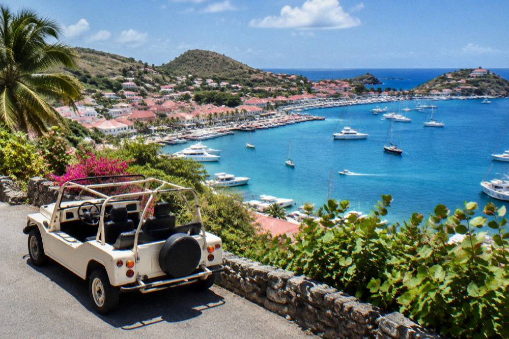 A small open-top rental car parked on a hillside road above the sea