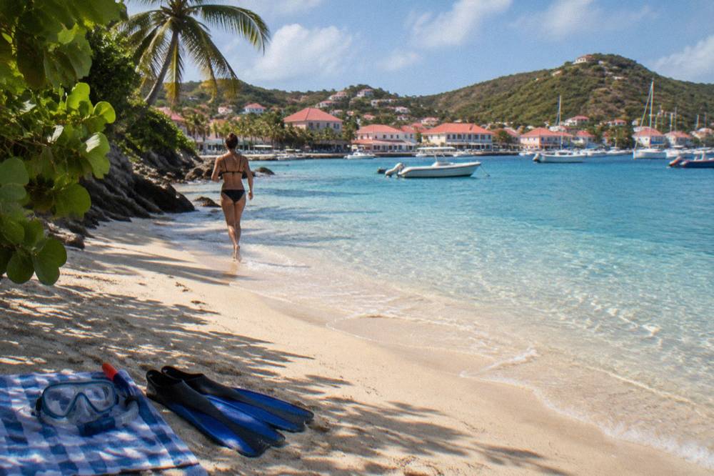 Snorkel mask and fins resting on a towel beside a calm sandy cove with clear shallow water