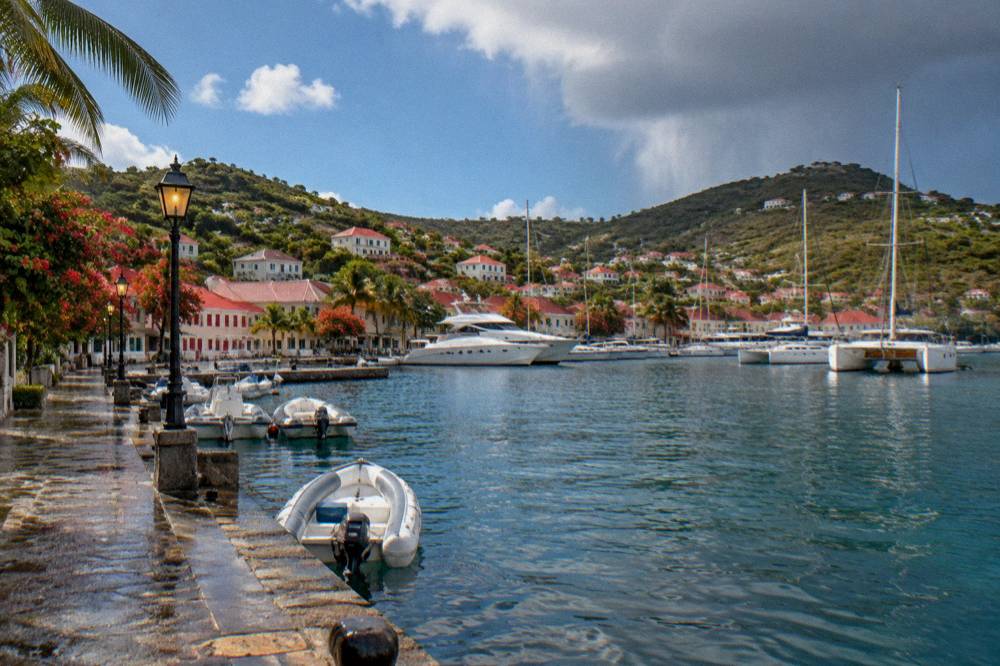 White yachts moored in a harbor at dusk with hillside lights and a lantern-lit stone quay