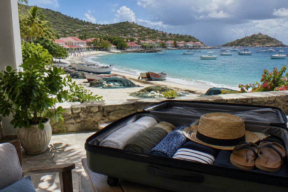 An open suitcase on a villa terrace with rolled clothing, a straw hat and a pair of sandals packed neatly