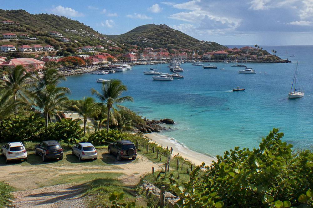 Cars parked at a grassy road end near a beach entrance among palm trees on St Barts