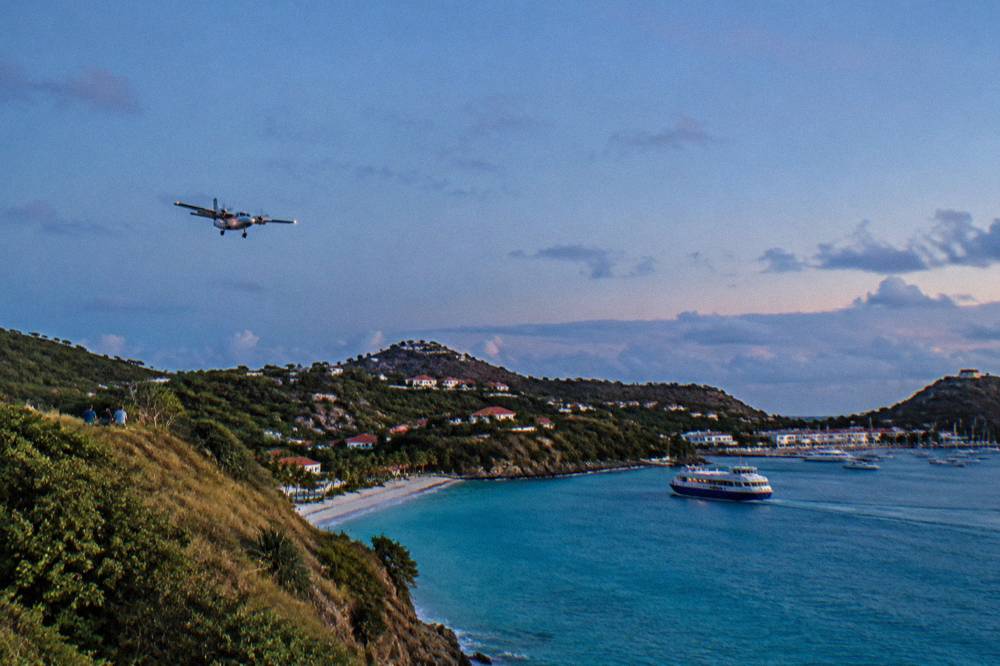 A ferry boat approaching a small harbor with white buildings and palm trees along the shore