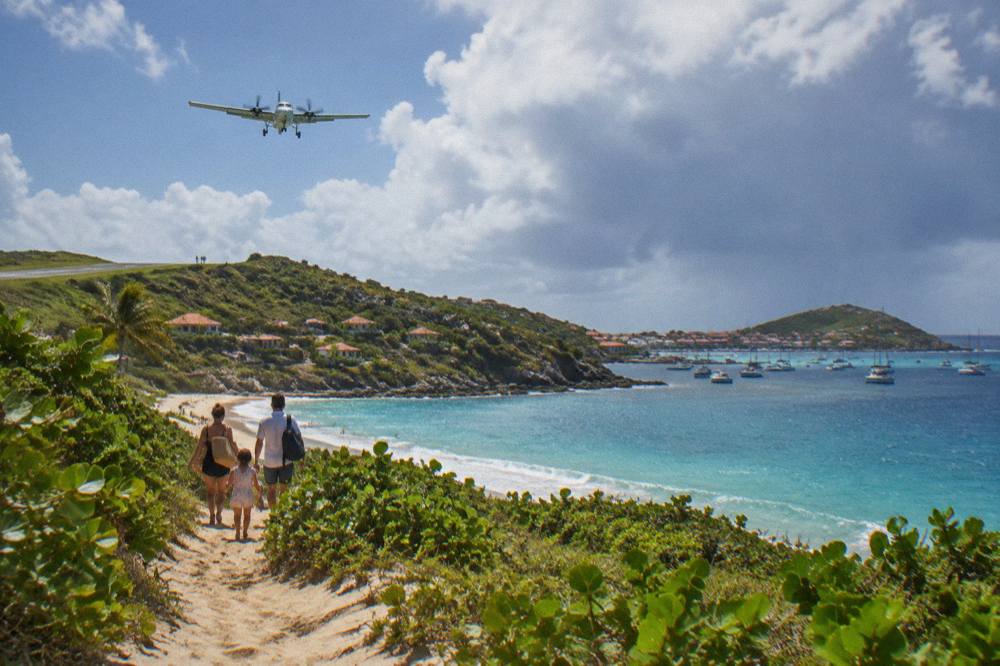 A family walking along a sandy beach path lined with low green vegetation toward the sea