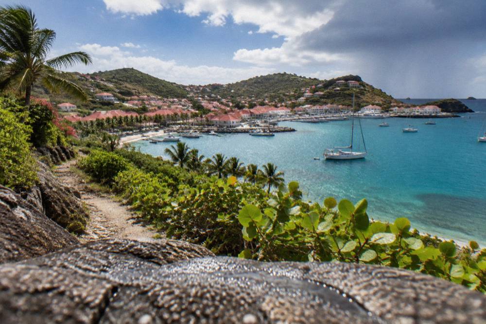A wooded coastal trail winding above a turquoise bay with a moored sailboat