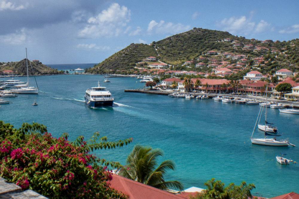 A passenger ferry approaching a small harbour with hills behind it