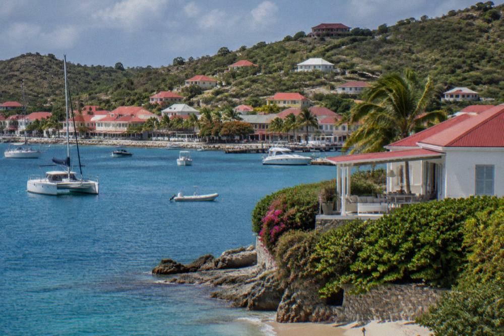A whitewashed villa with a red roof and a shaded terrace above the sea