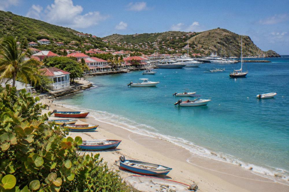 Small wooden fishing boats on a sandy beach beside a village on St Barts