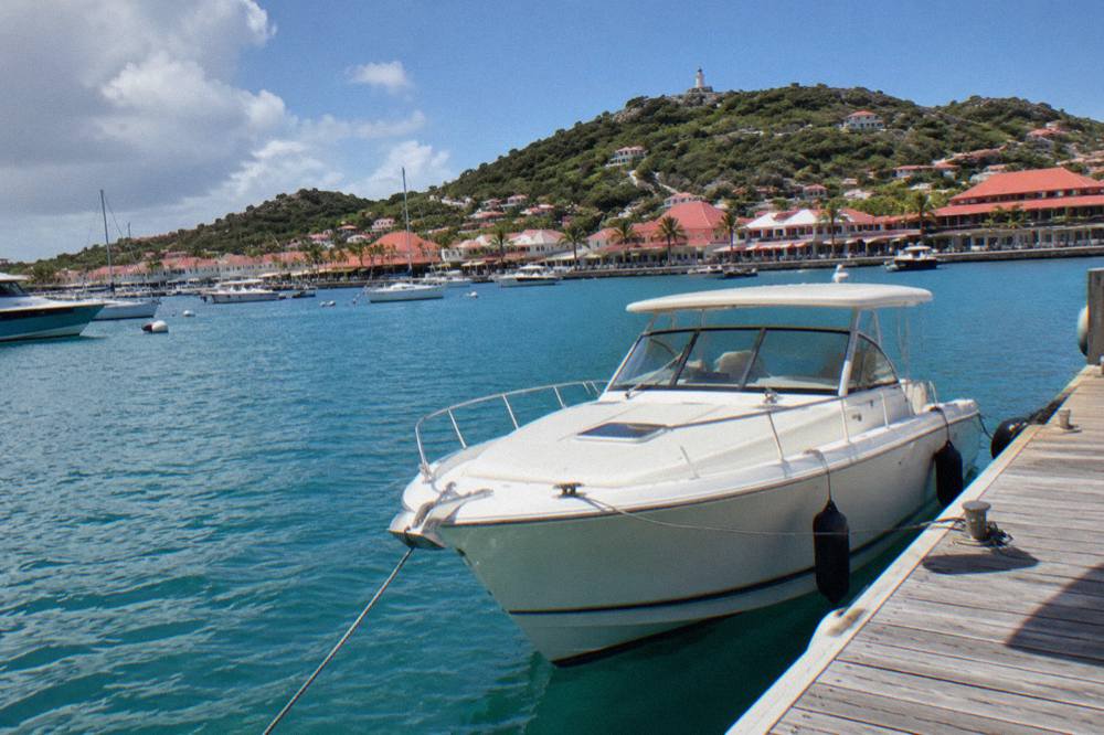 A sleek white charter boat moored at a wooden dock in a small Caribbean marina