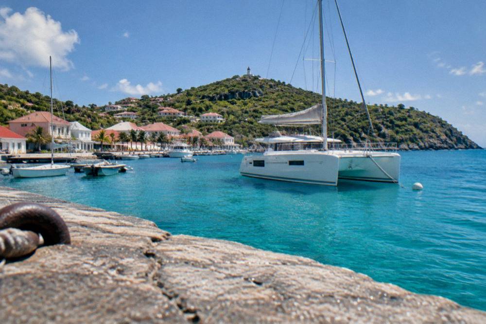 A catamaran anchored in clear turquoise water beside a wooded headland