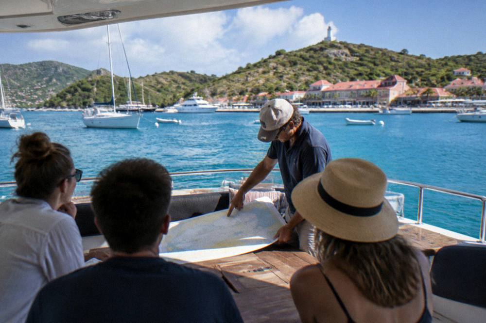 A captain pointing at a chart while passengers listen on the aft deck of a boat