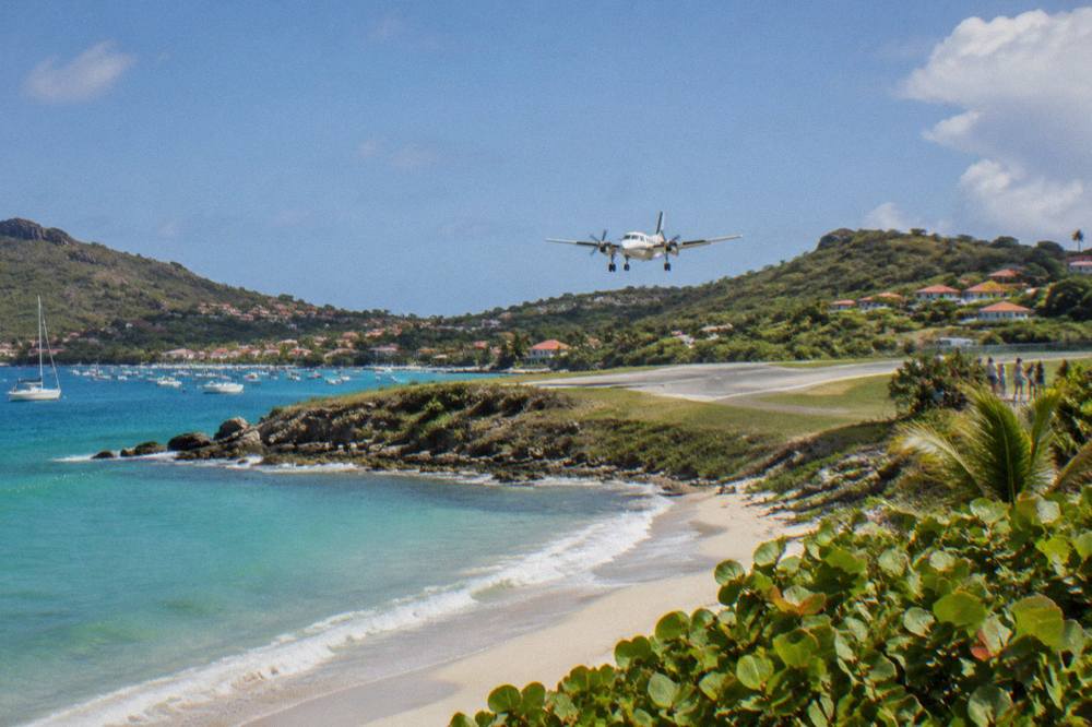 A small turboprop aircraft on a short runway between a beach and green hills