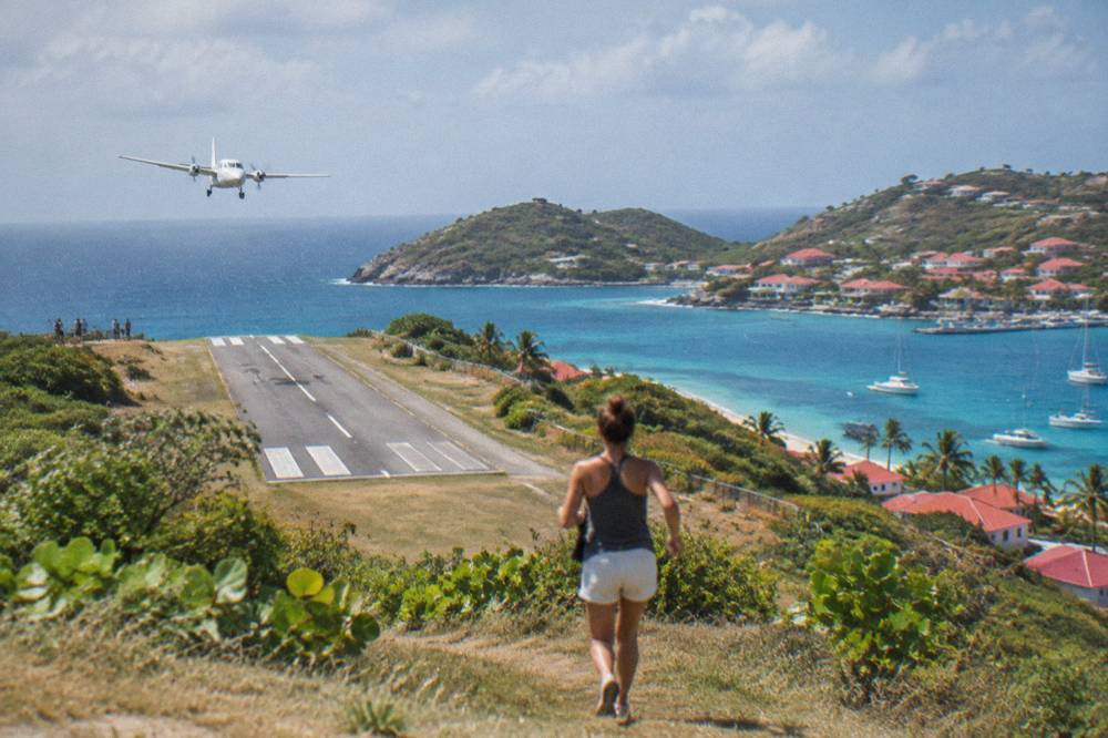 A light aircraft banking over blue Caribbean water toward a small green island