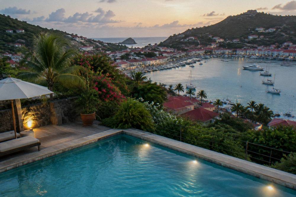A villa swimming pool at dusk with lights reflecting on the water and hills behind